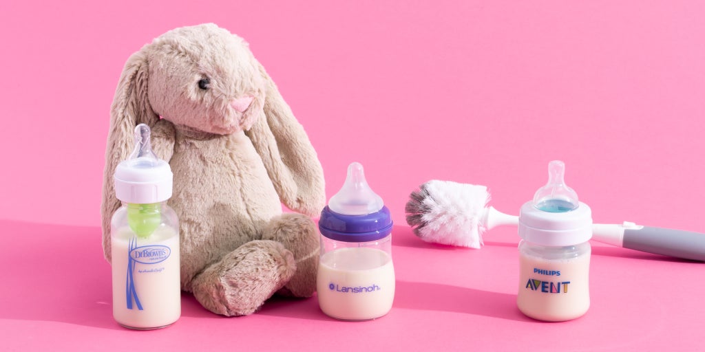 Three baby bottles along with a bottle brush and a stuffed animal.