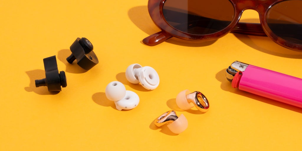 Our three picks for best earplugs for concerts, including our pick the Loop Experience 2 earplugs, alongside a pair of sunglasses and a lighter.